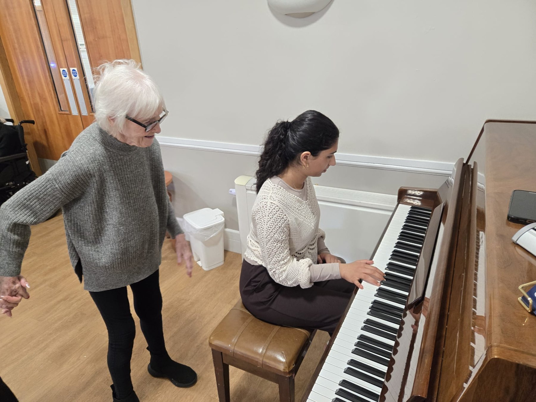 Sophia playing piano with a resident standing nearby